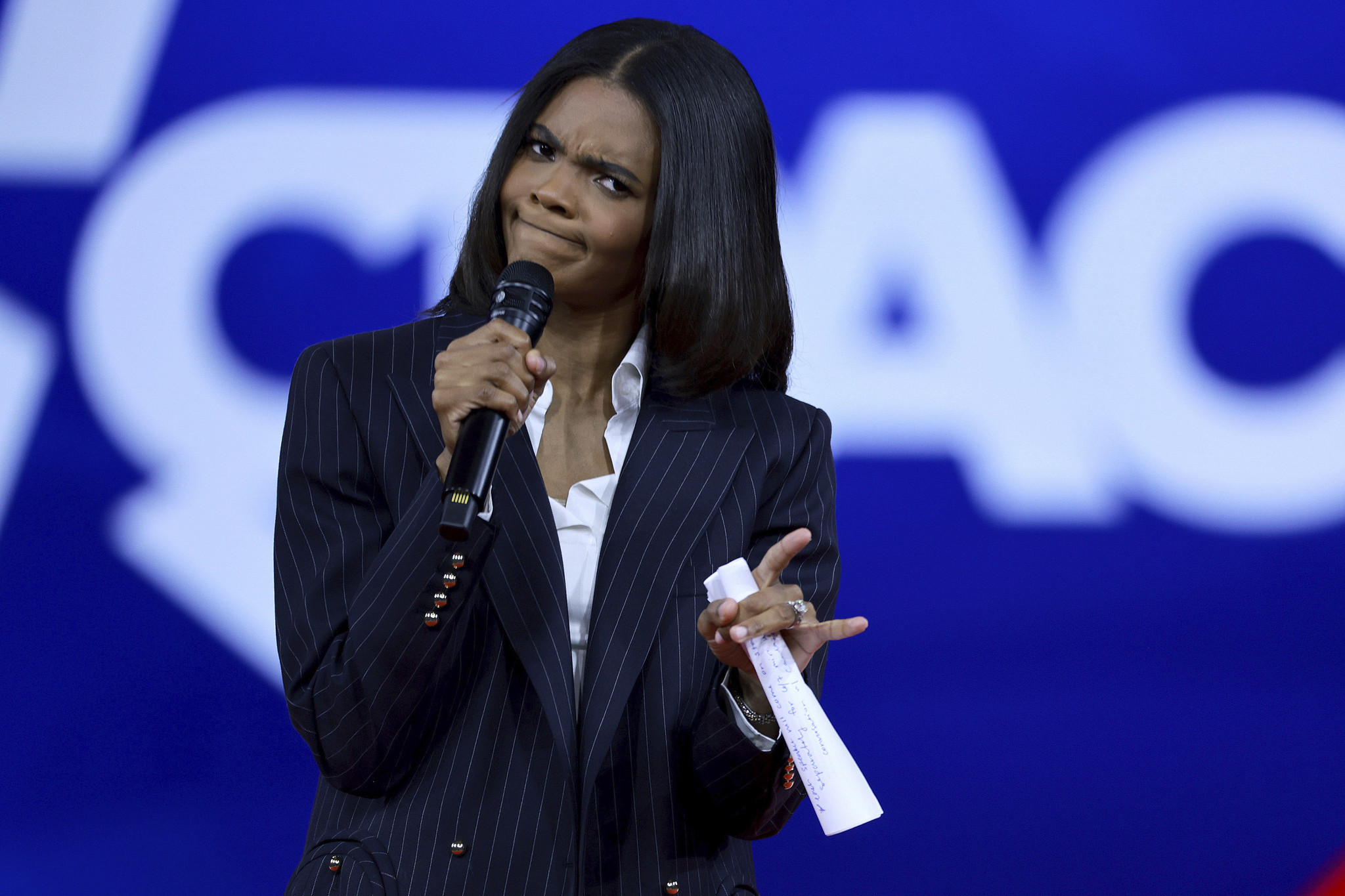 Candace Owens speaking at a public event in 2026, photographed at a lectern in a crowded venue