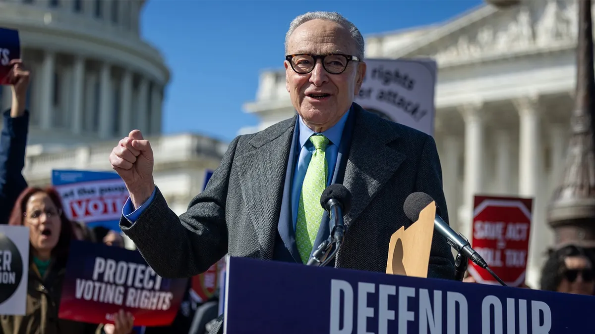 Chuck Schumer speaking at an outdoor rally near the U.S. Capitol with microphones in front of him and the Capitol visible in the background, news photography style