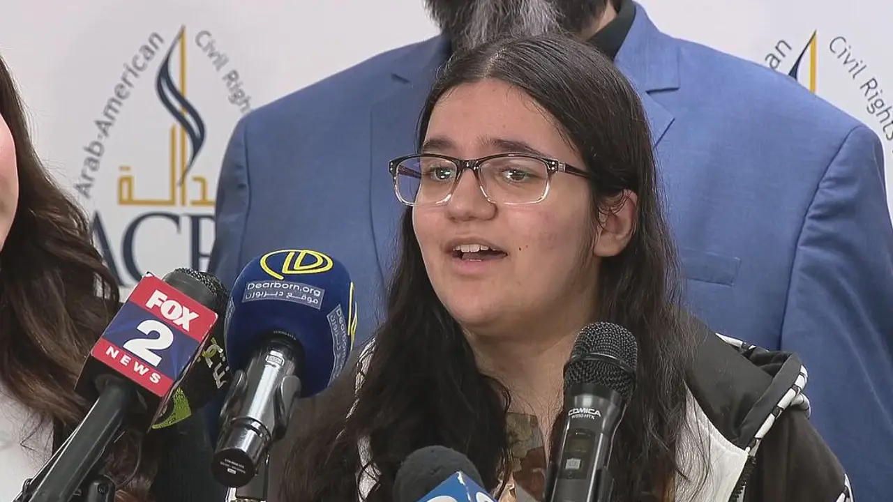 Danielle Khalaf standing in a school hallway with classroom doors behind her, natural light from windows, documentary news photography style