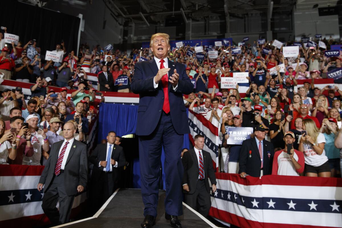 Donald Trump speaking at a campaign event with supporters and American flags visible, editorial news photo style