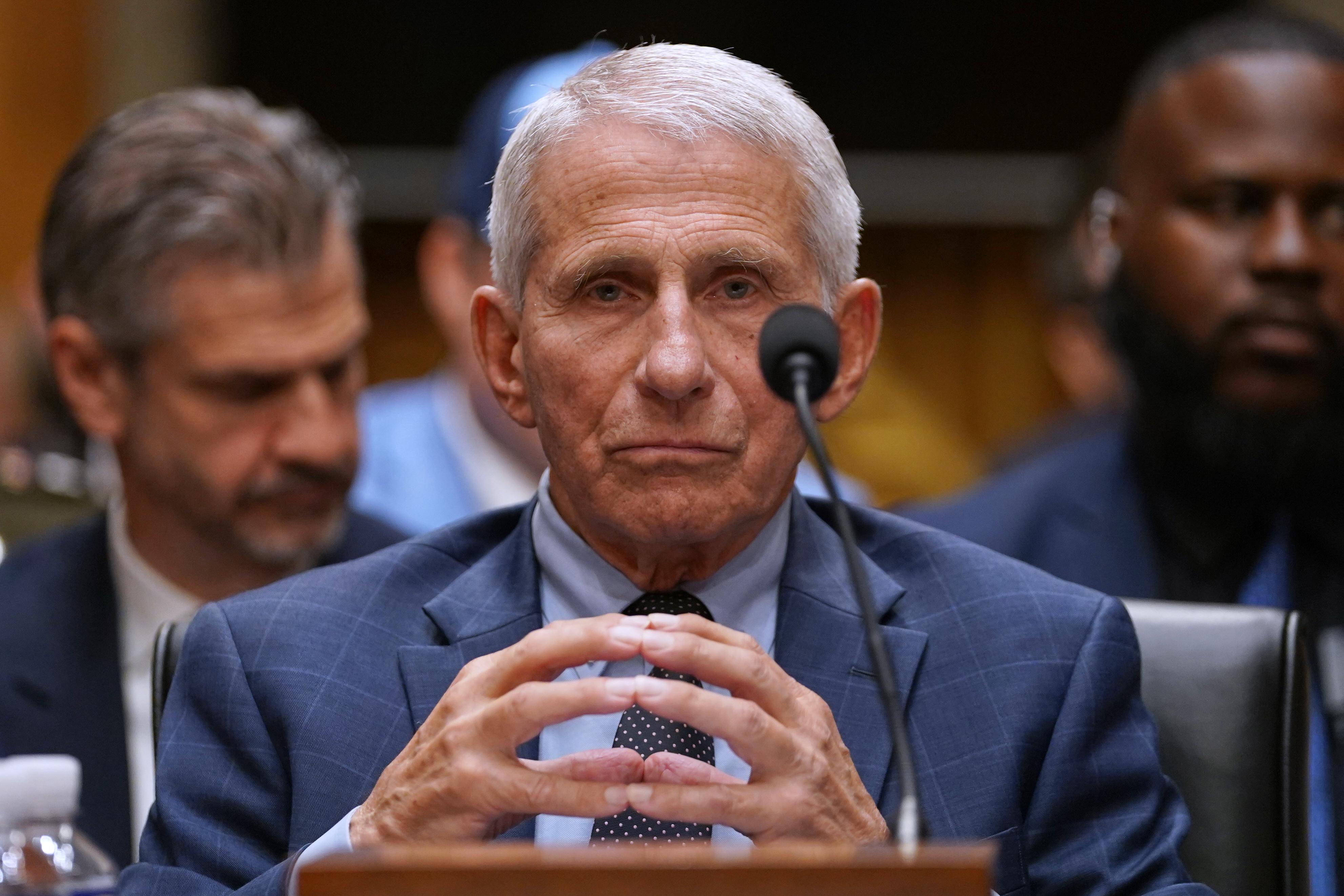Dr. Anthony Fauci seated at a witness table during a U.S. Senate committee hearing, facing senators and microphones in a formal hearing room