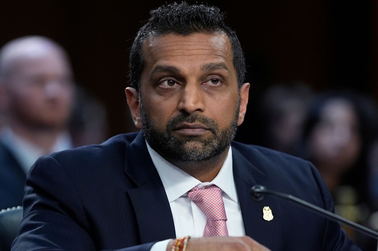 FBI Director Kash Patel testifies at a congressional hearing table with microphones and a nameplate.