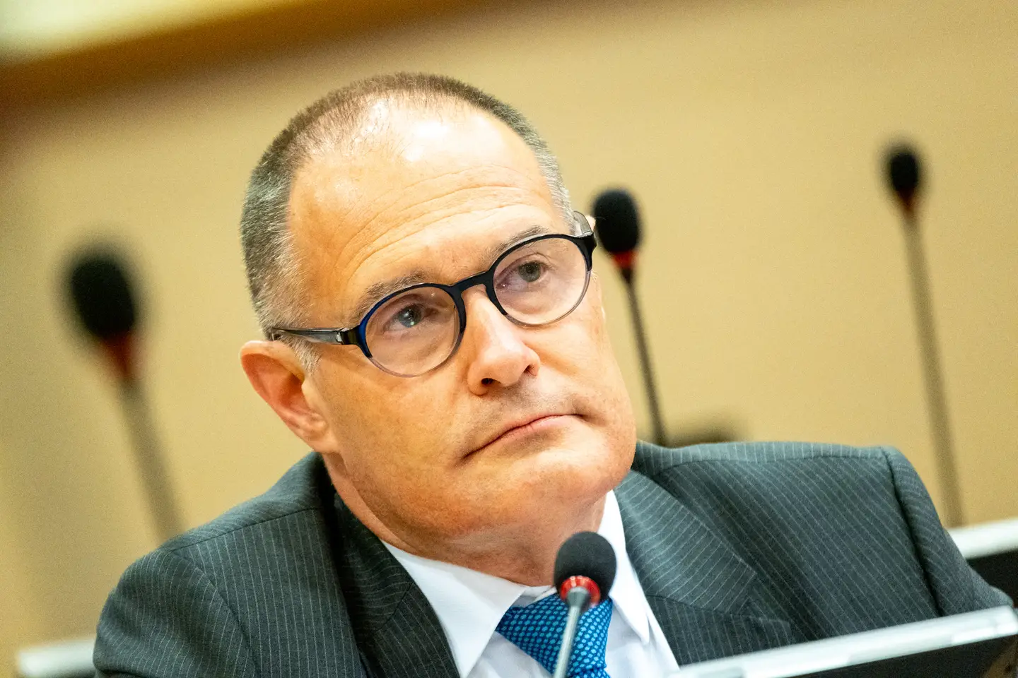 Fabrice Leggeri speaking at a public political event in France with microphones in front of him and audience members blurred in the background, news photography style