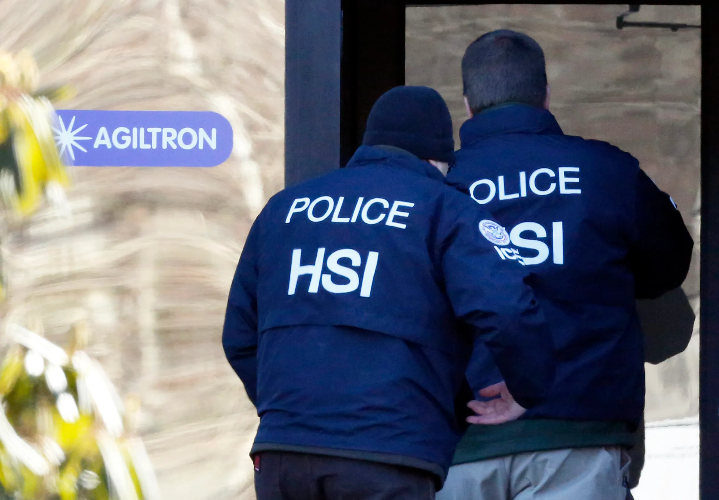 Federal immigration enforcement agents in tactical gear standing near vehicles during an enforcement operation, with faces not clearly identifiable