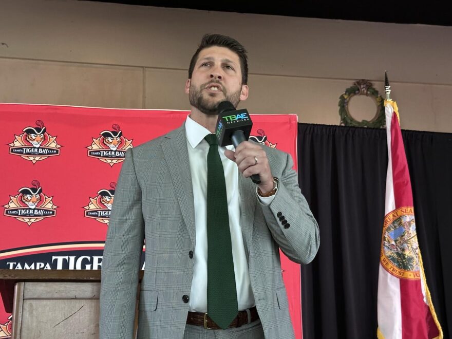Florida Attorney General James Uthmeier speaking at a podium during a press conference, with microphones in front of him, news photography style