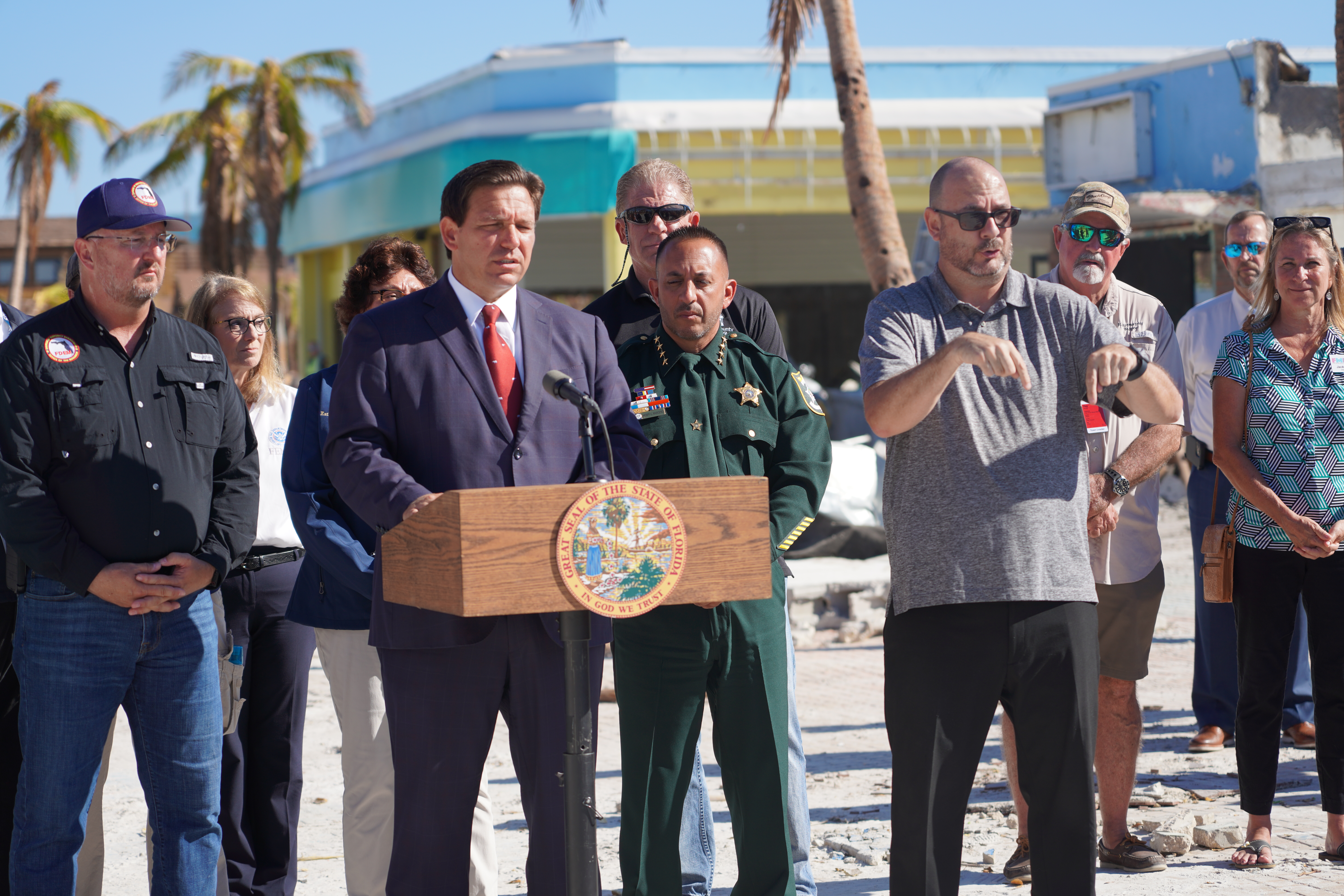 Florida Gov. Ron DeSantis speaking at a podium during a public event in Florida, with U.S. and Florida flags visible nearby