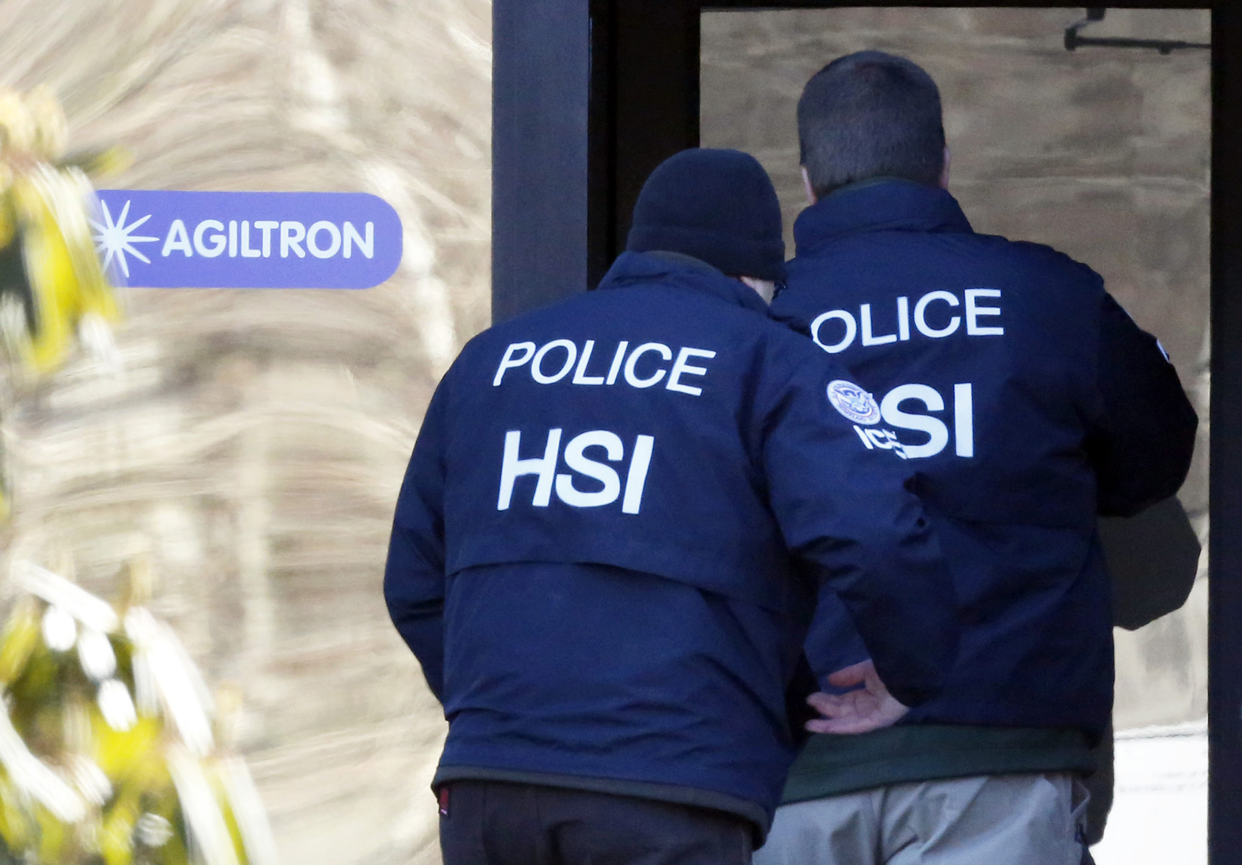 Homeland Security Investigations agents in jackets walking near a government building entrance during a public-facing operation