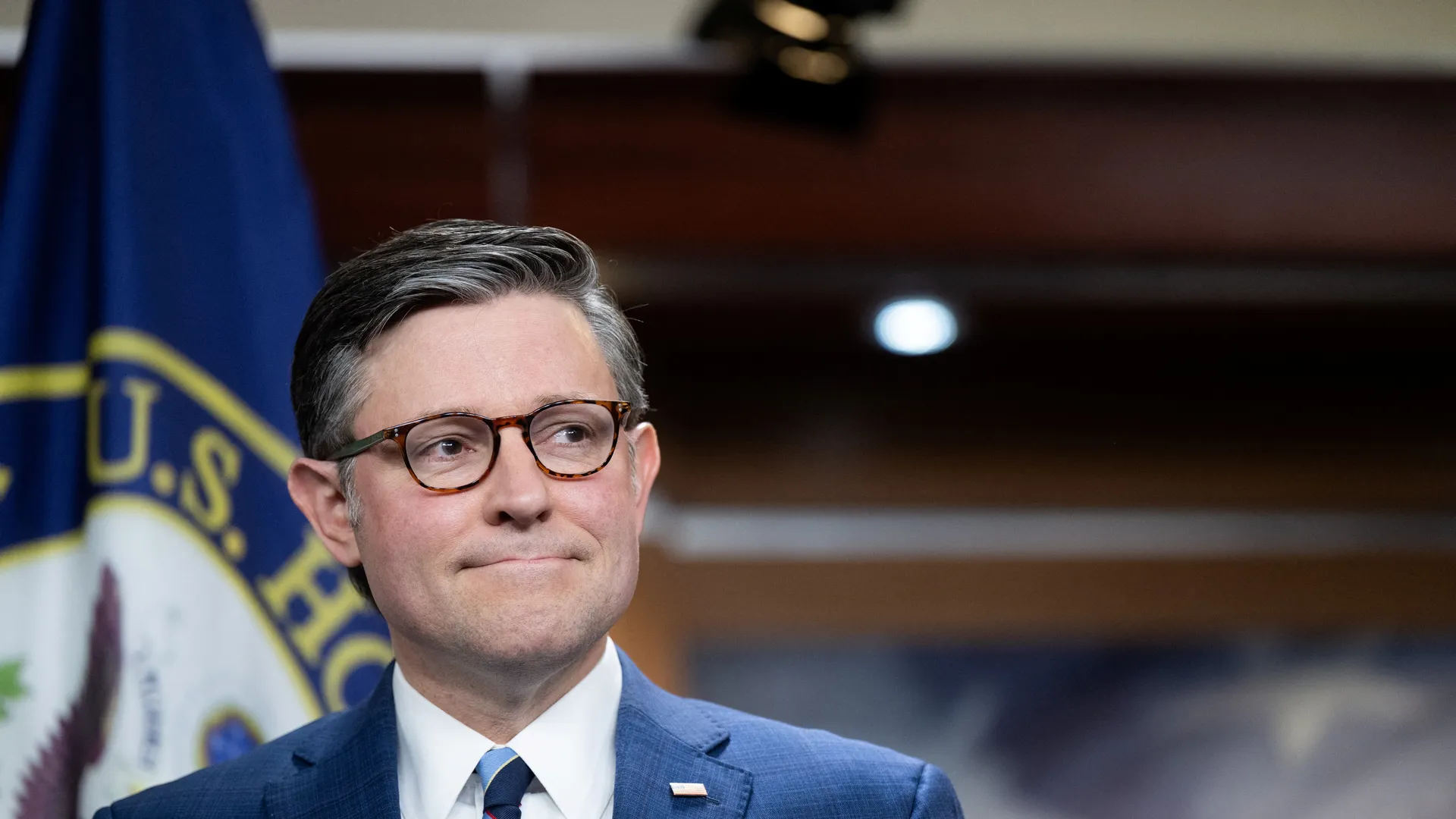 House Speaker Mike Johnson speaking at a Capitol press microphone cluster, reporters and cameras in front of him, news photography style