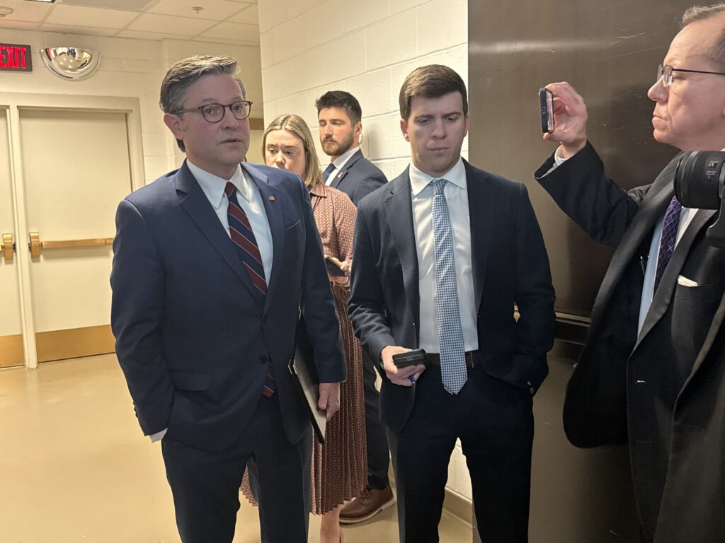 House Speaker Mike Johnson speaking with reporters in a Capitol hallway at night, news photography style