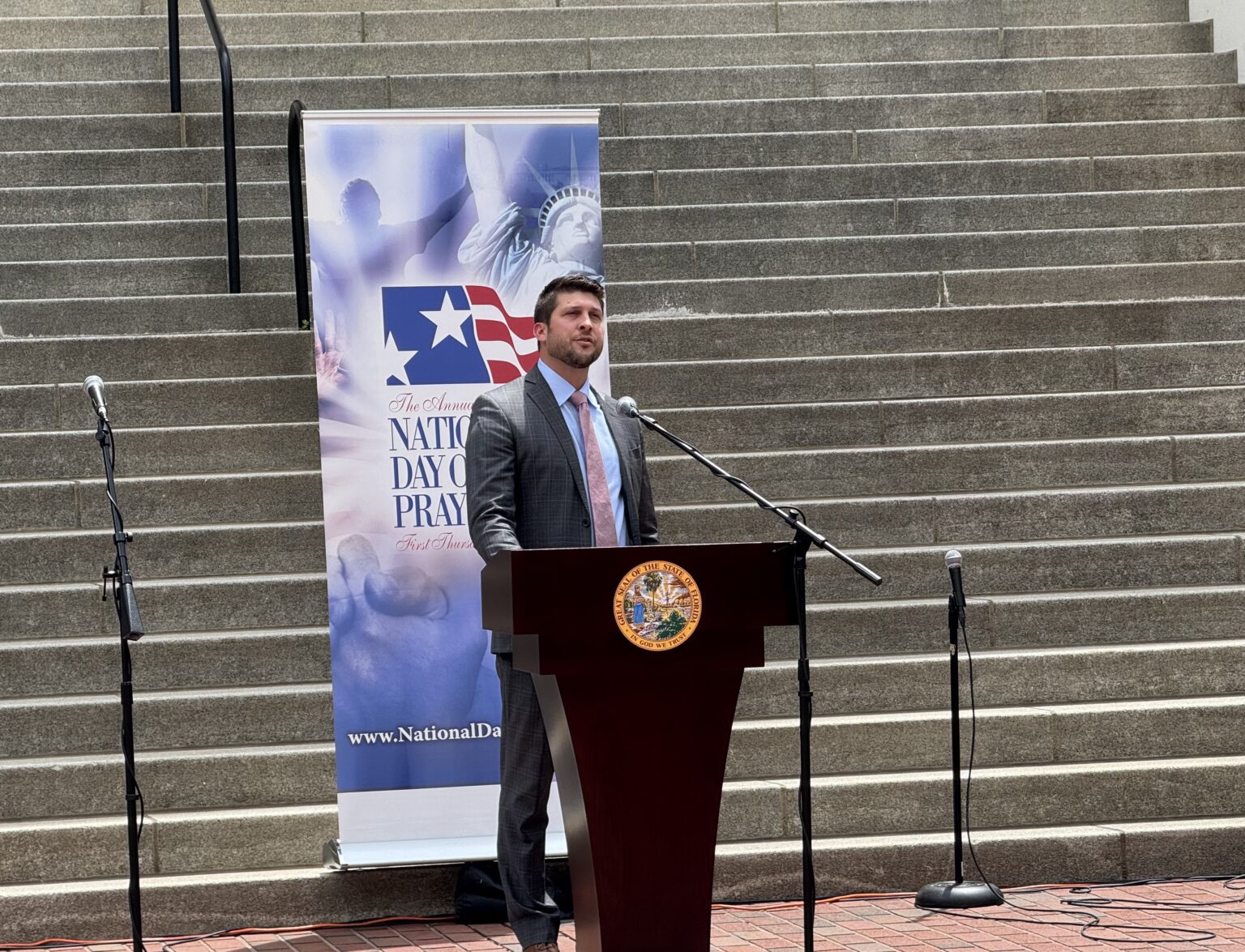 James Uthmeier, Florida attorney general, speaking at a podium during a press conference inside a state government building, news photography style