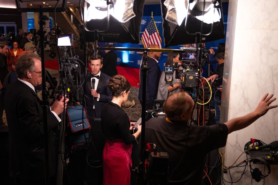 Journalists and event staff moving through a security screening area with magnetometers and bag checks at a Washington, DC venue entrance, news photography style