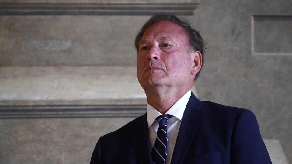 Justice Samuel Alito walking up the steps outside the Supreme Court building in Washington, D.C., with photographers in the background, news photography style