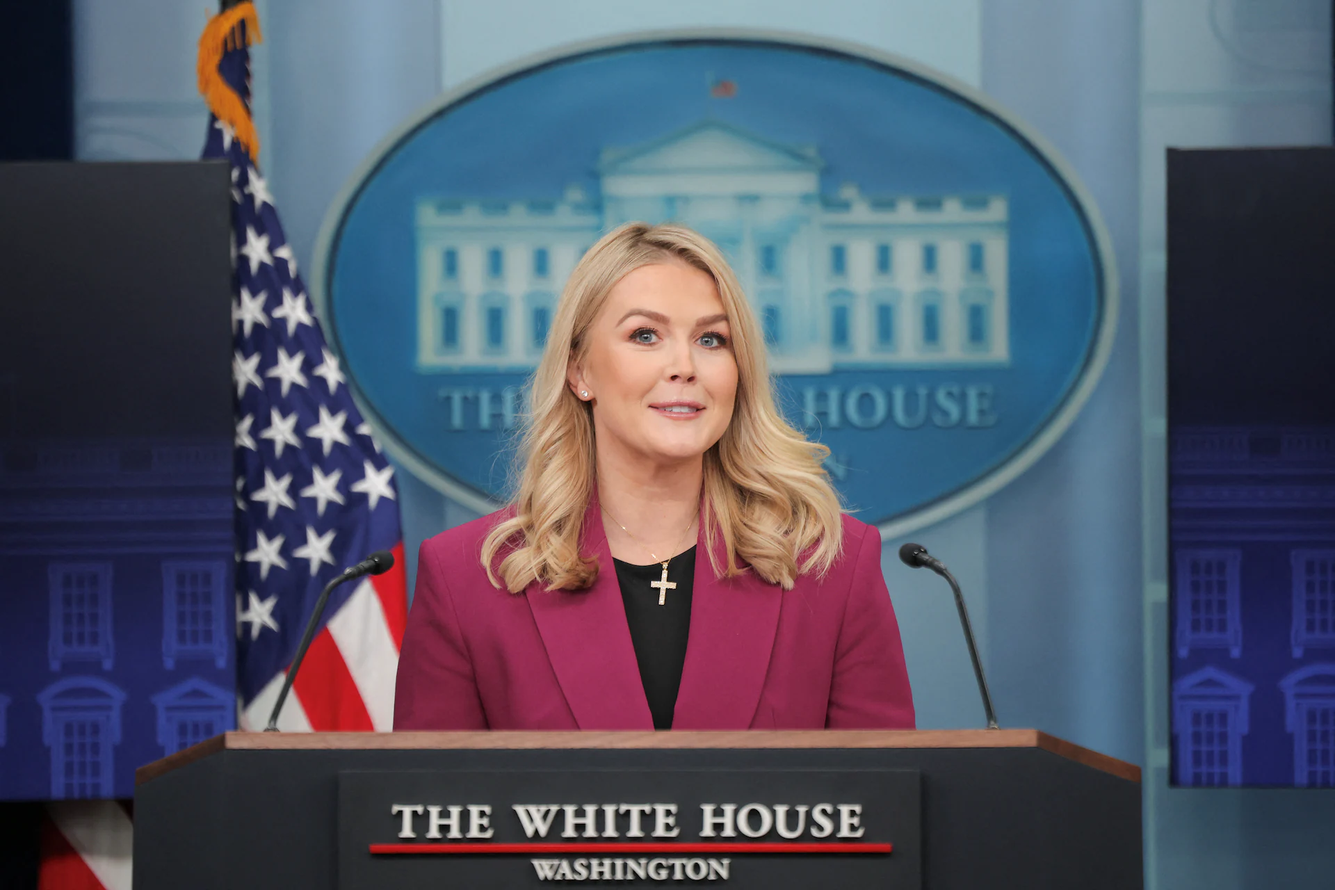 Karoline Leavitt speaking at a public event, facing cameras and reporters.