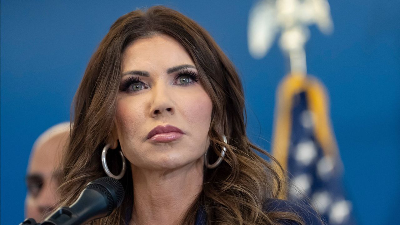 Kristi Noem speaking at a Department of Homeland Security lectern during an indoor press briefing, news photography style