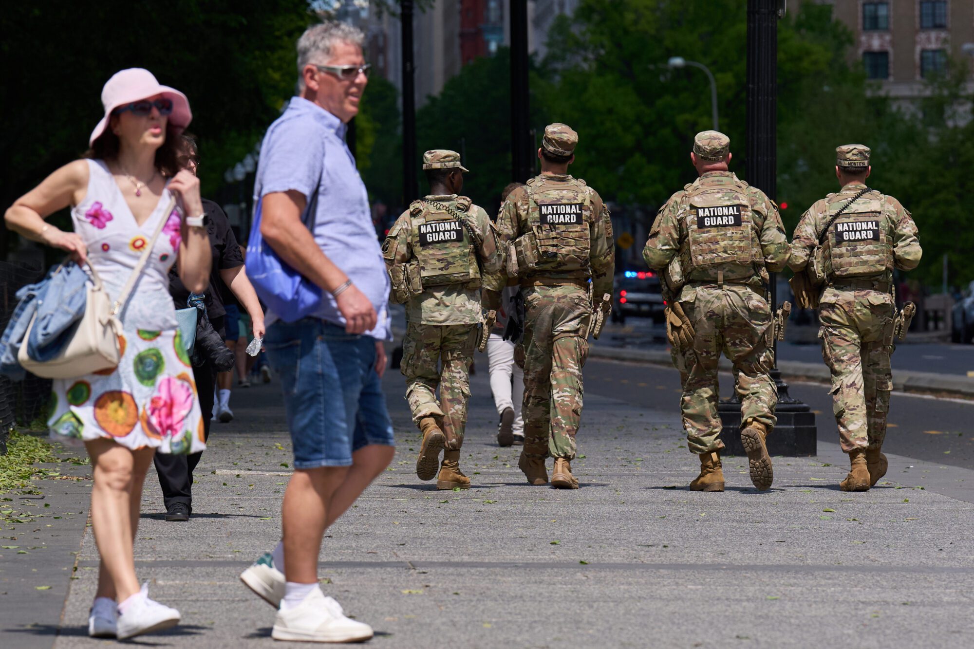 National Guard troops standing in a city street near police barricades during a public disturbance response, with civilian buildings in the background