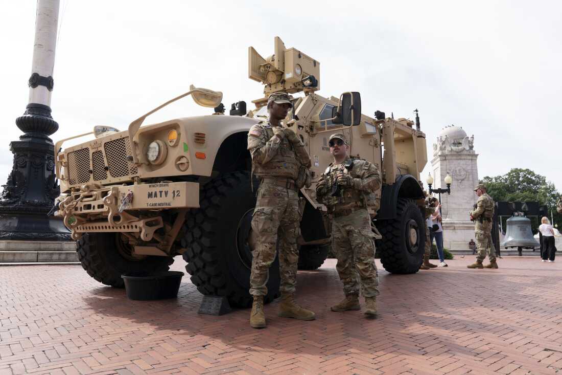 National Guard troops stationed near prominent federal buildings in Washington, D.C., with uniforms and vehicles visible in a real street setting