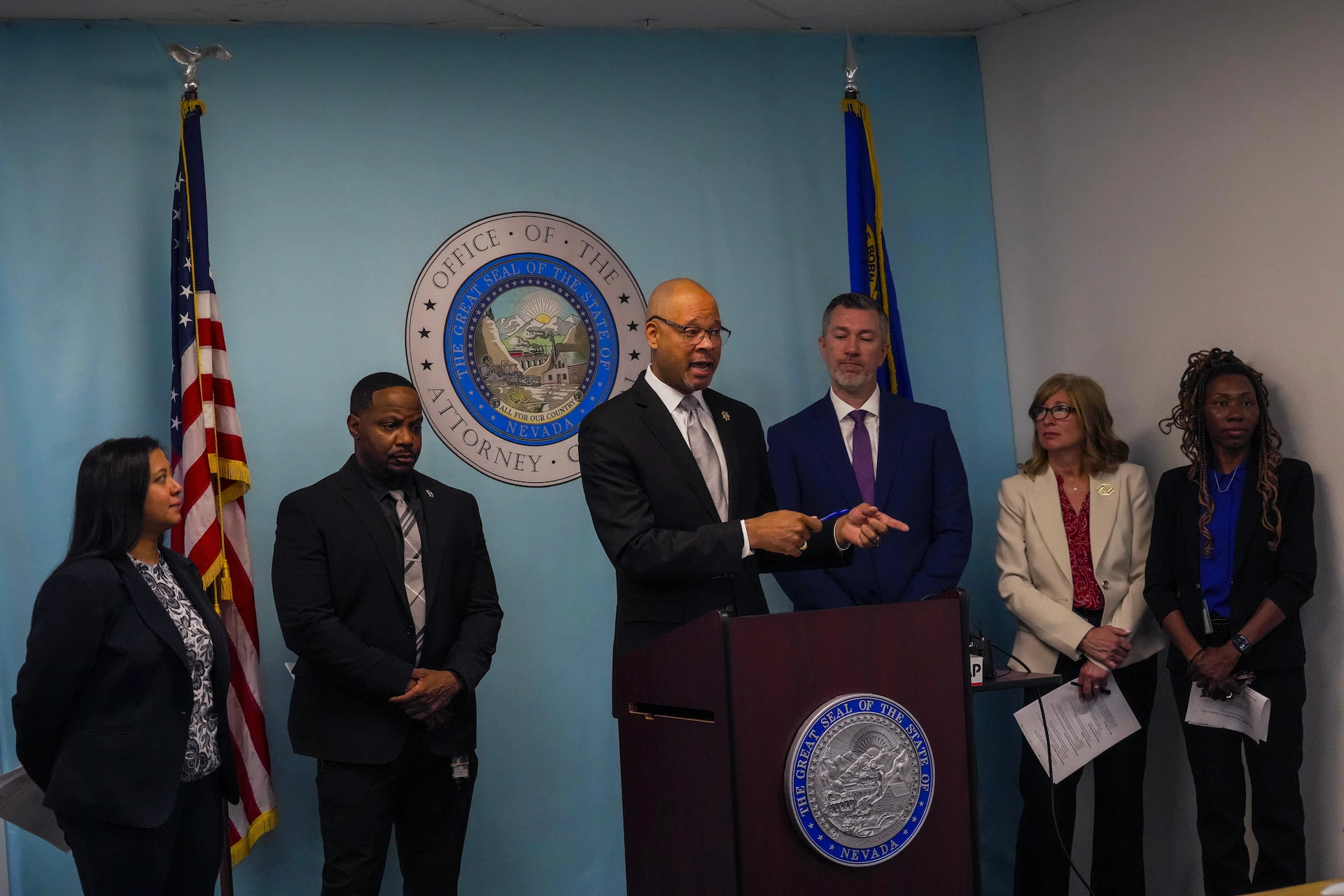 Nevada Attorney General Aaron Ford speaking at a podium during a press conference, with microphones in front of him, news photography style