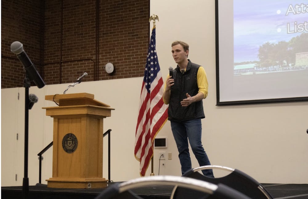 New Hampshire state Rep. Sam Farrington speaking at a lectern on the House floor during a legislative debate, candid news photography style