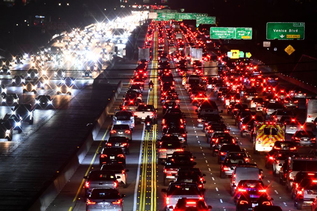 Nighttime traffic on an American interstate with headlights and taillights flowing past, photographed from an overpass in a realistic news style