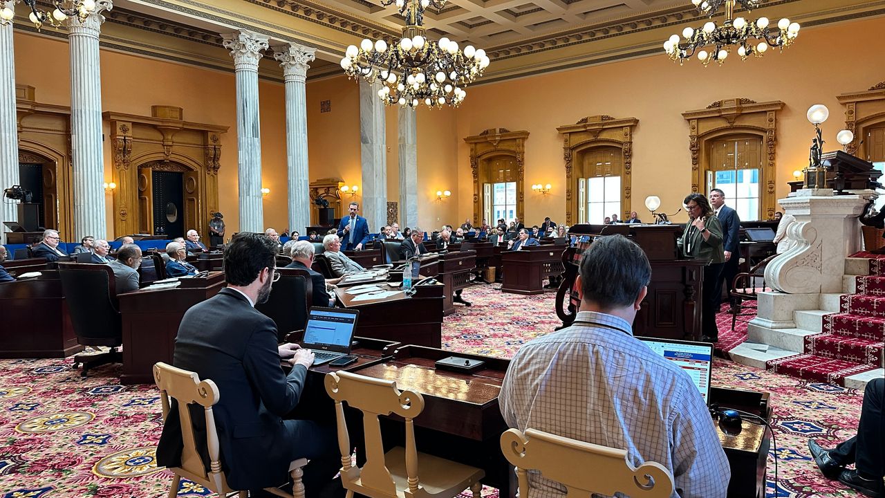 Ohio senators seated at their desks during a floor session in the Ohio Senate chamber in Columbus, with voting boards lit, news photography style