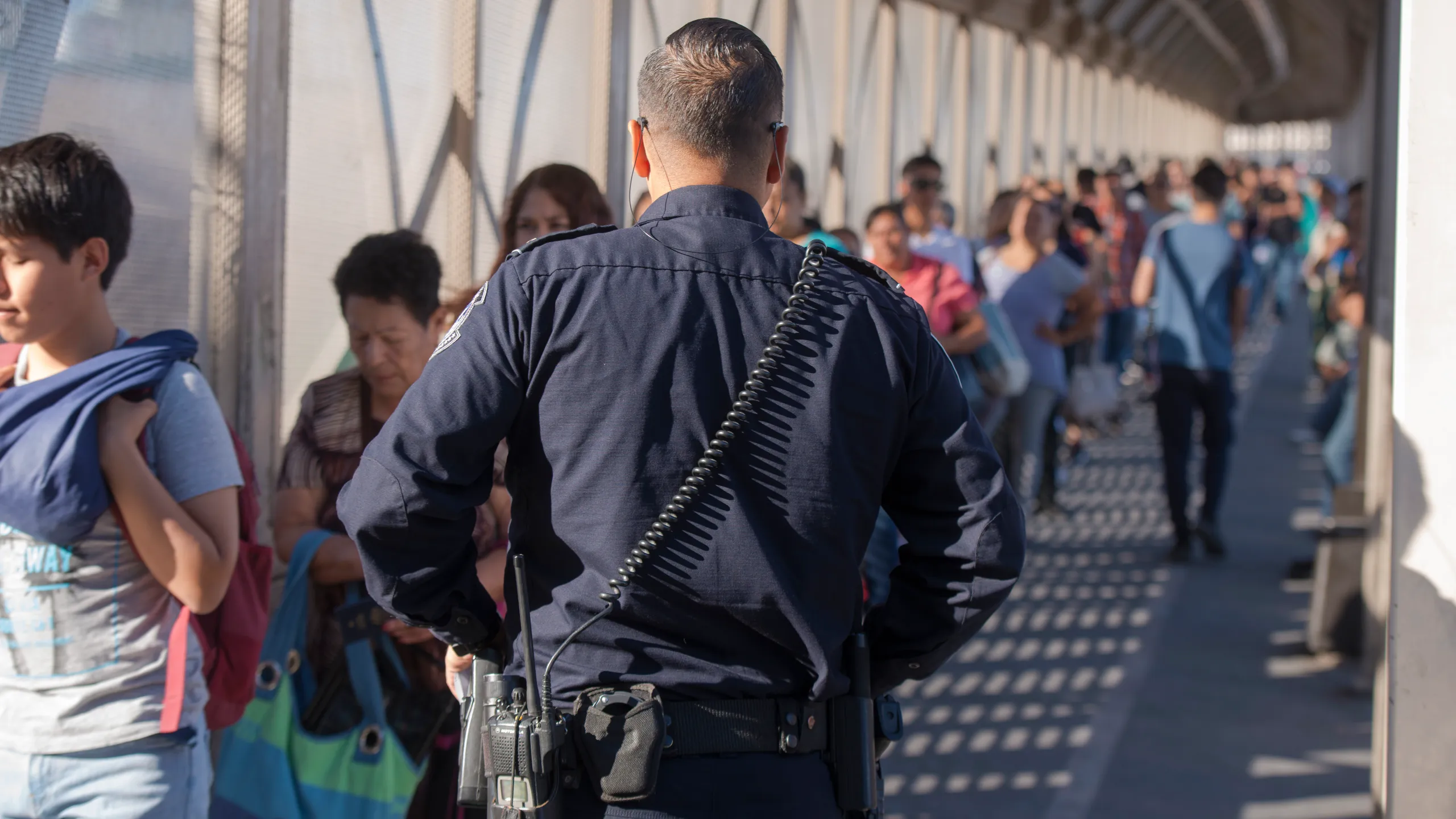People standing in a pedestrian line at a U.S. border crossing checkpoint in Texas, daytime news photography style