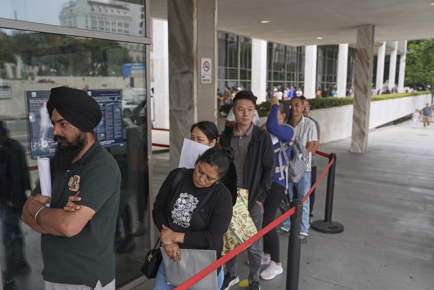 People waiting in line outside a federal building for an immigration-related appointment in a U.S. city, candid news photography style
