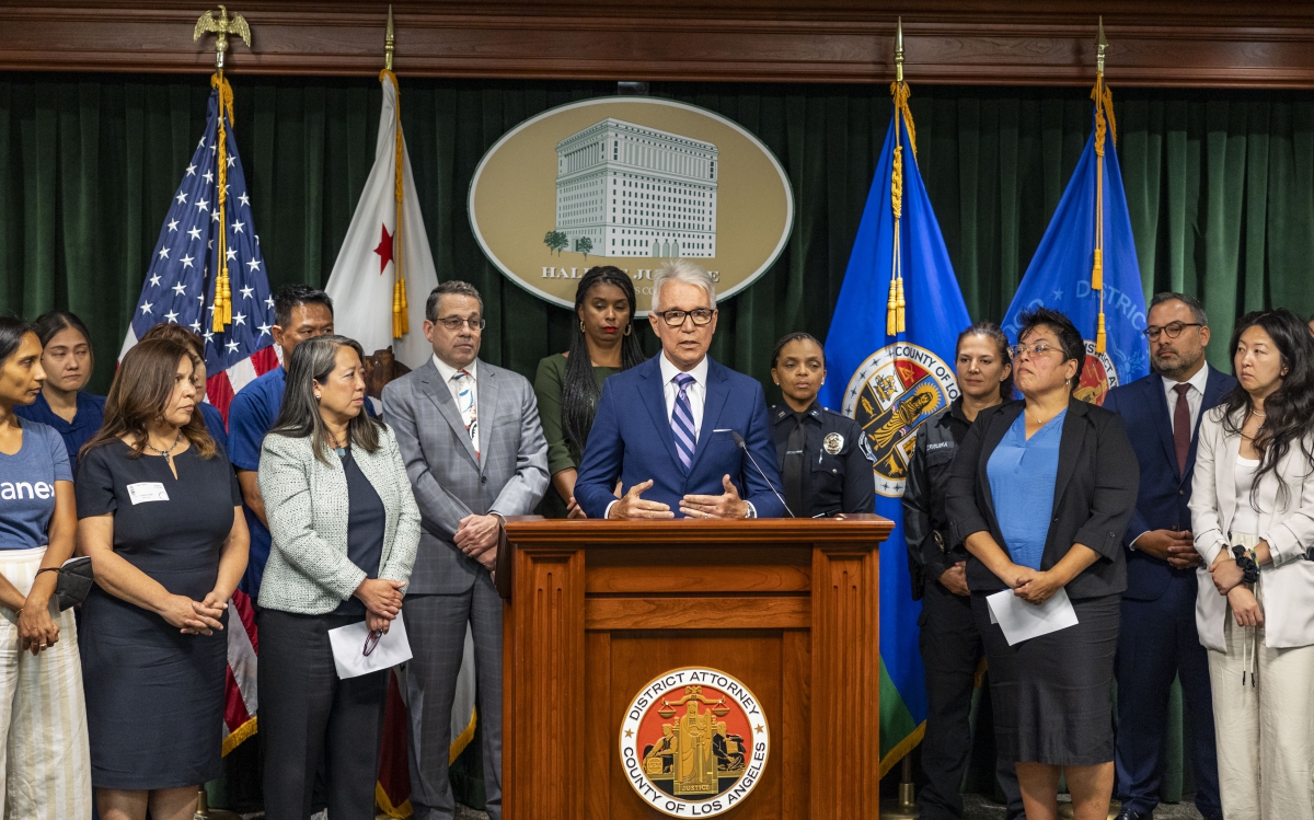 Philadelphia District Attorney Larry Krasner speaking at an outdoor podium, surrounded by microphones.