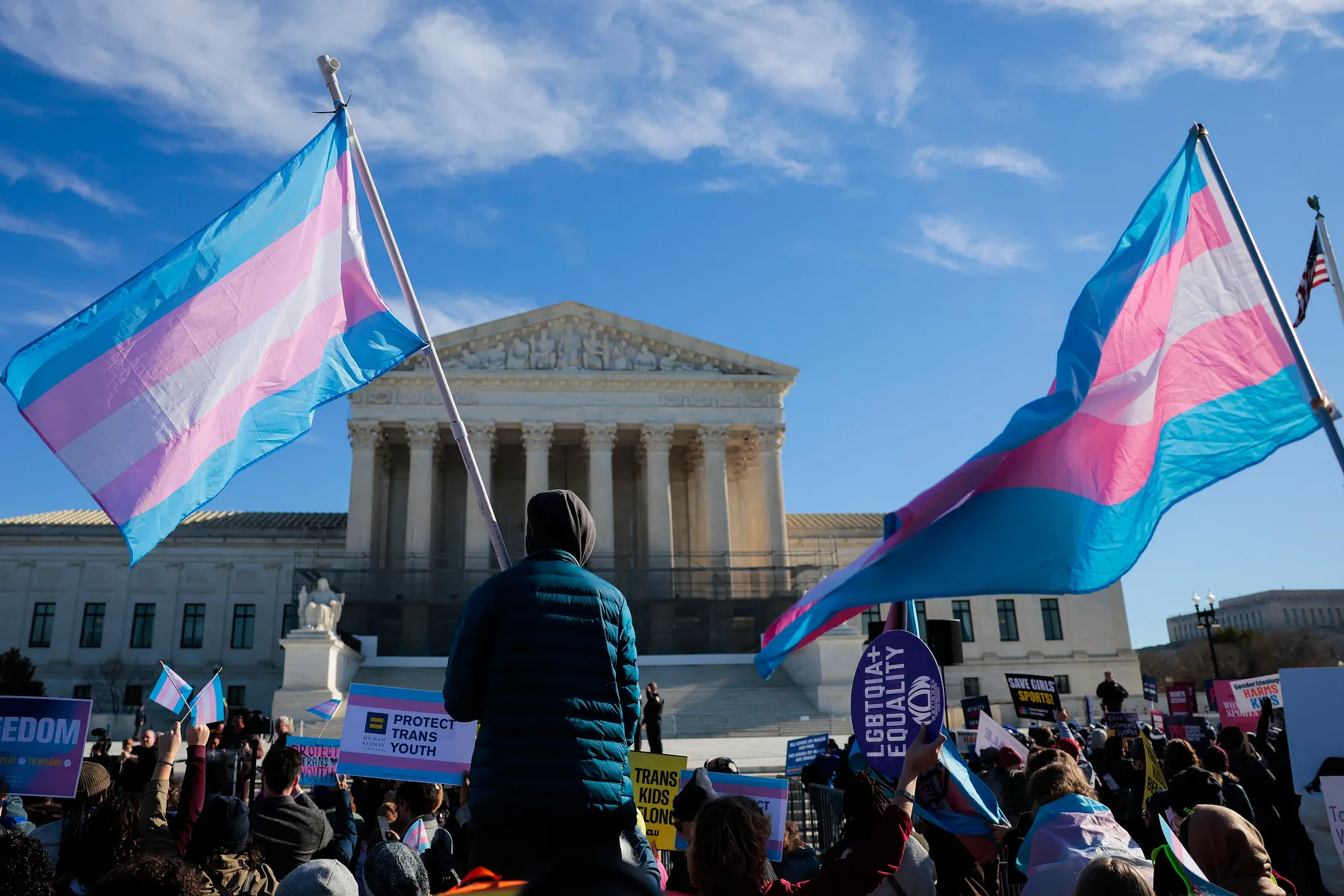 Photograph outside the United States Supreme Court with demonstrators holding transgender pride flags on a cold winter day in Washington, D.C., news photography style