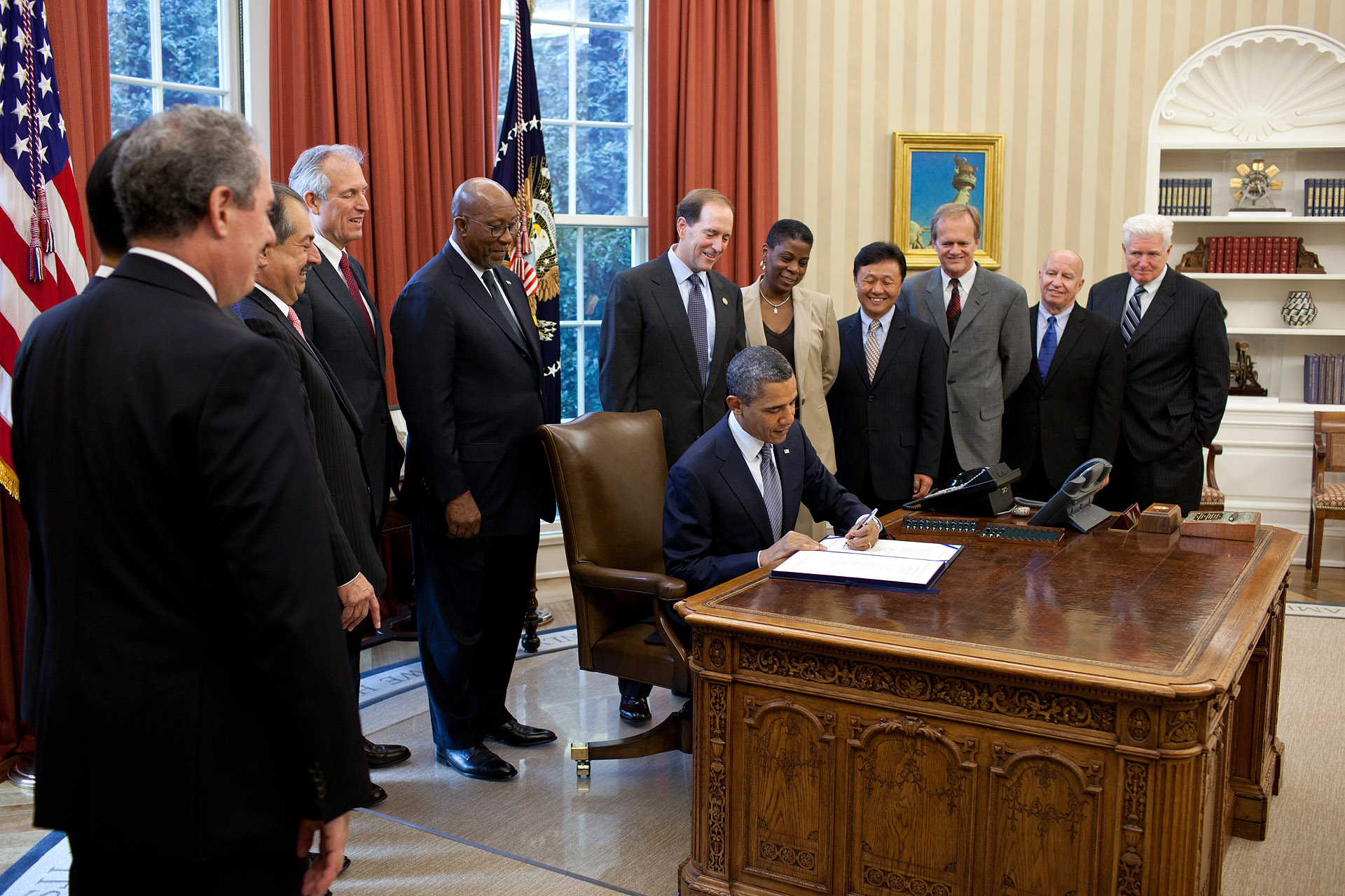 President Barack Obama at a White House desk signing a bill into law with several members of Congress standing behind him, candid news photograph