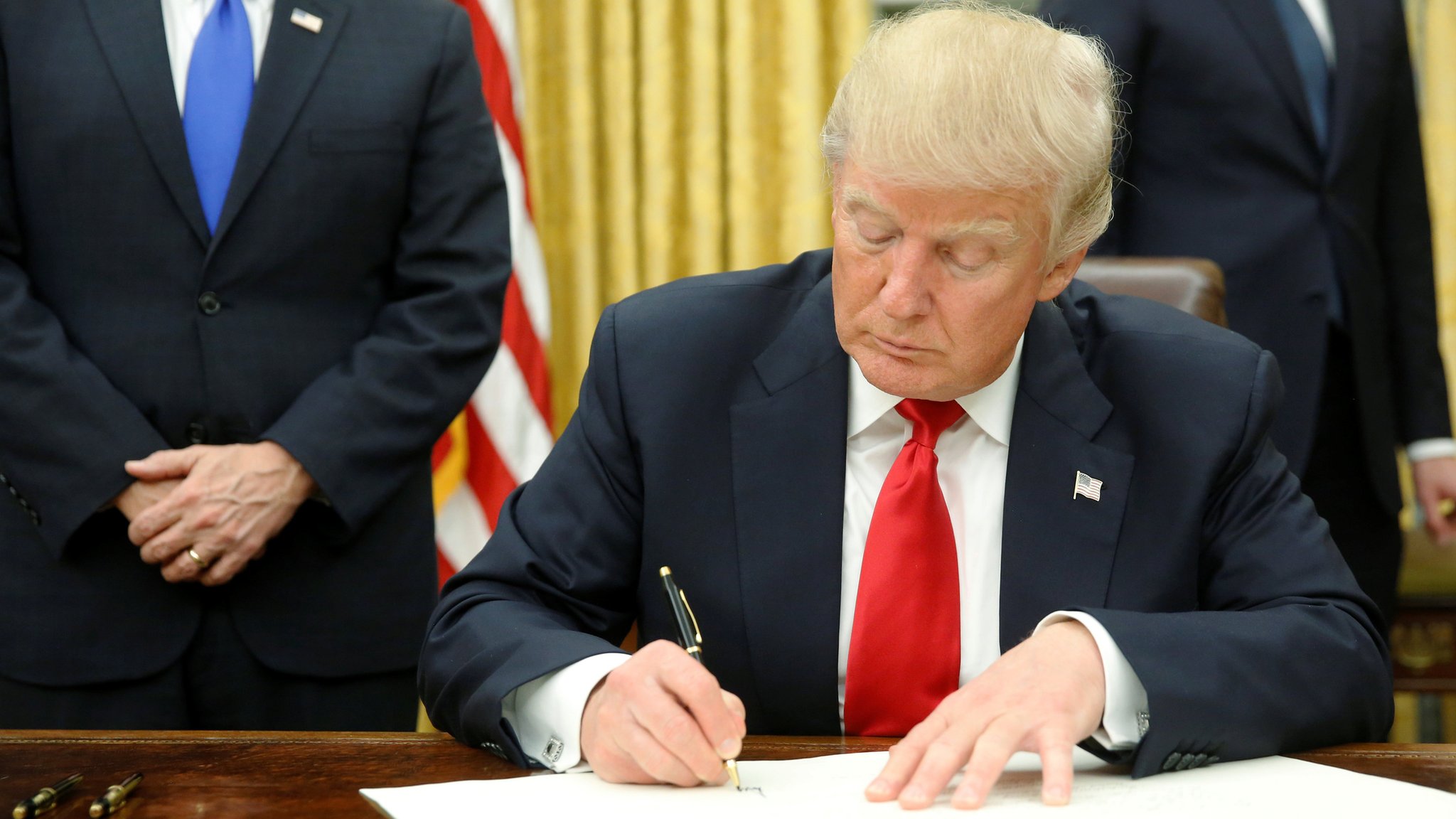 President Donald Trump at the Resolute Desk in the Oval Office as he signs a stack of executive orders