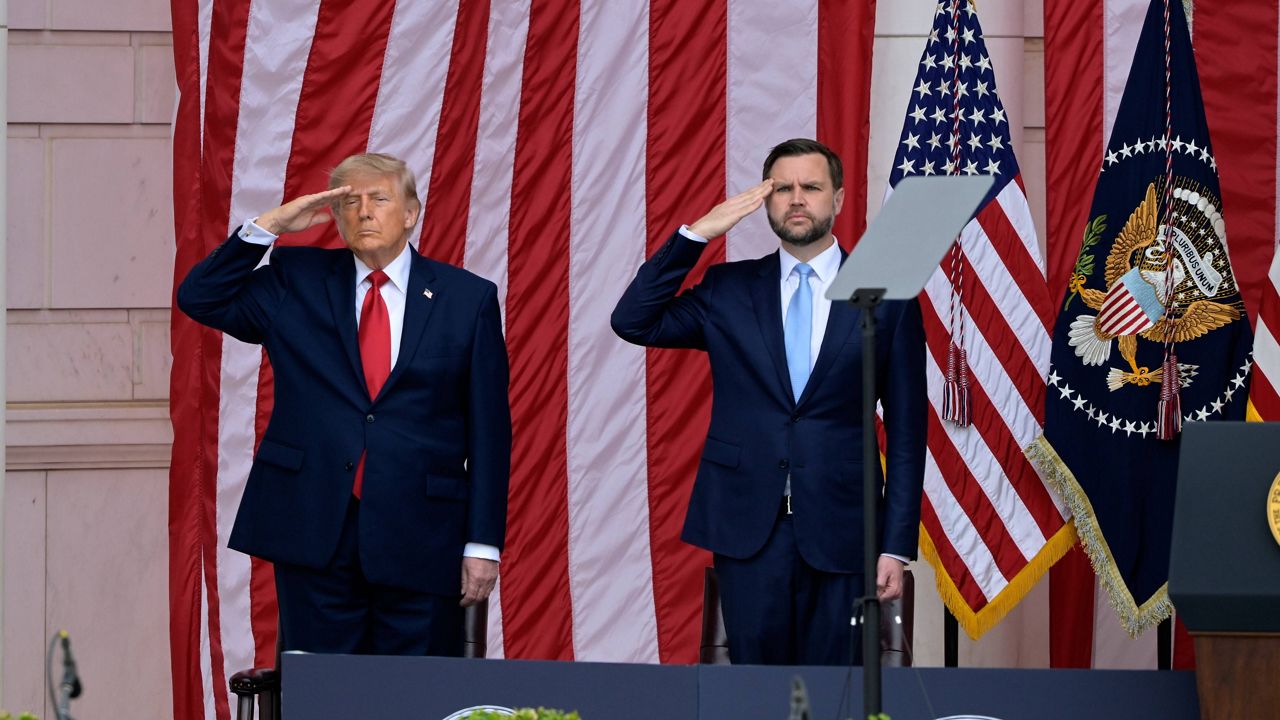 President Donald Trump saluting during a Memorial Day ceremony at Arlington National Cemetery, formal outdoor setting with uniformed military present, news photography style