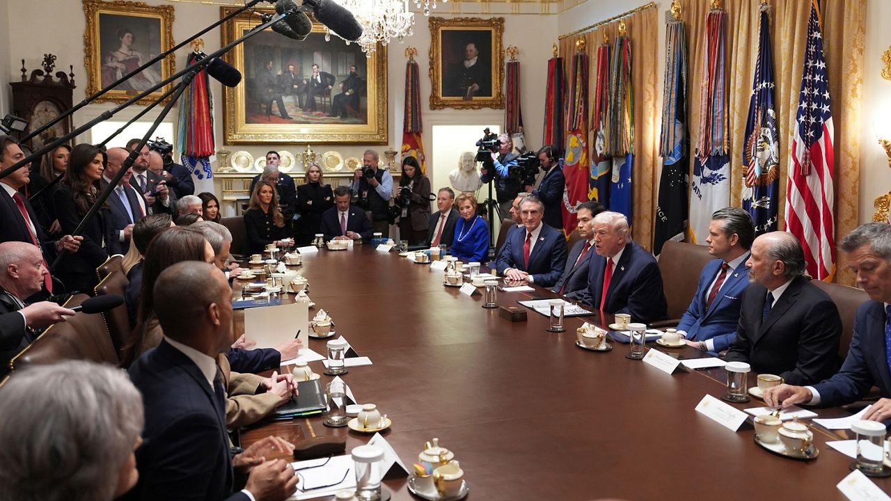 President Donald Trump seated at a conference table in the White House with aides nearby, candid news photography style