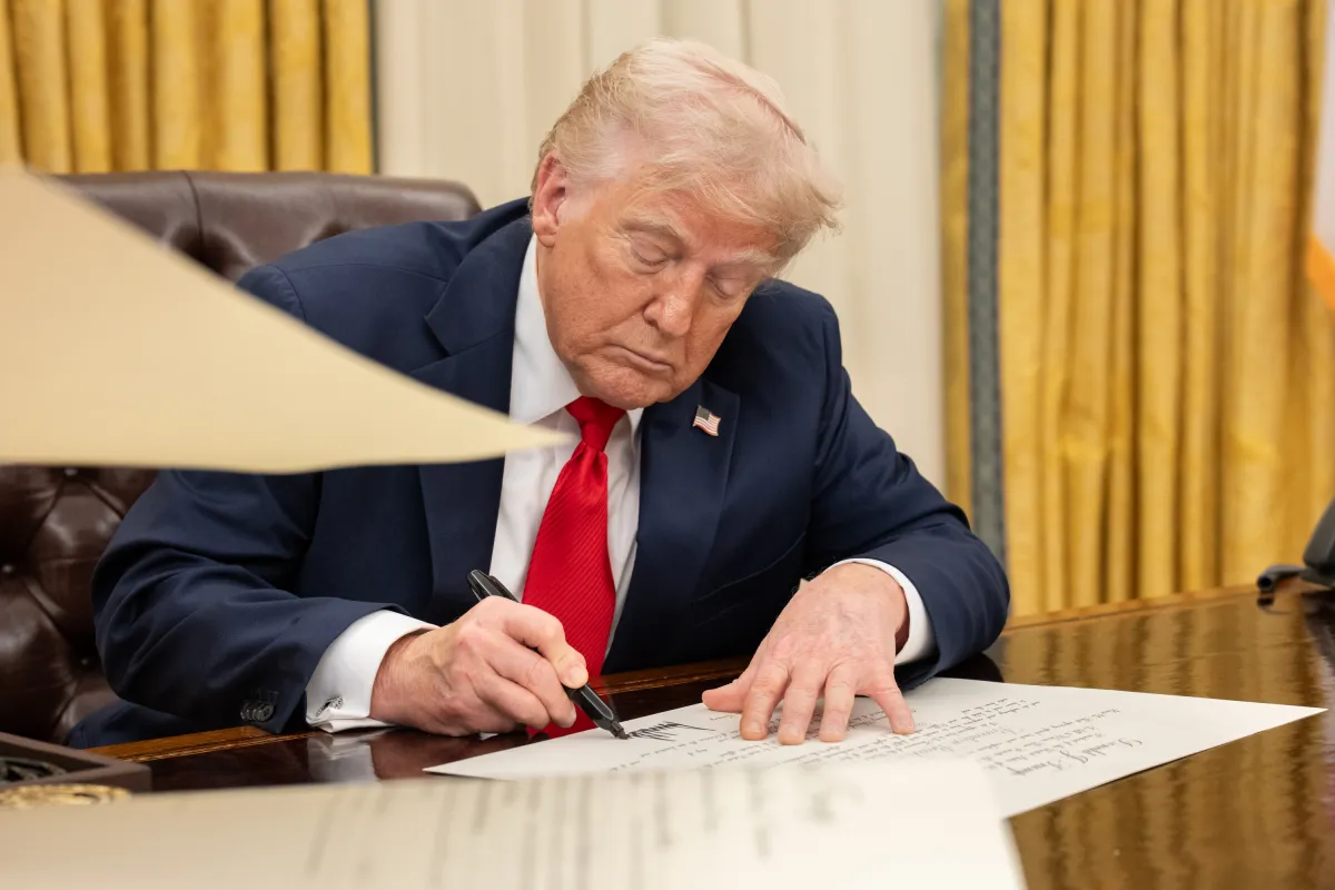 President Donald Trump seated at the Resolute Desk in the Oval Office during an executive order signing, official event photo