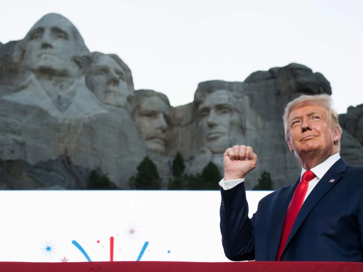 President Donald Trump speaking at an outdoor podium, with Mount Rushmore visible behind him during a public appearance
