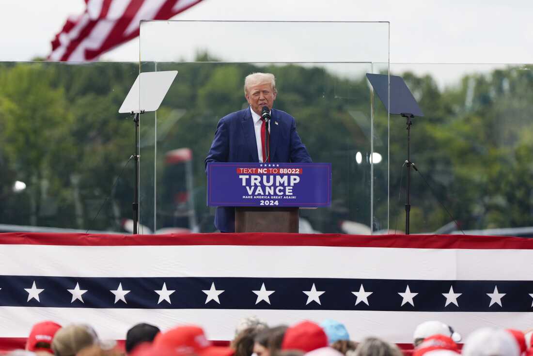 President Donald Trump standing at a podium at an indoor campaign rally, speaking to a crowd, news photography style