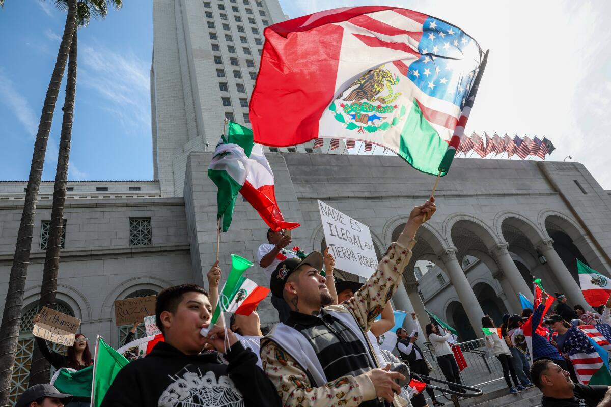 Protesters gathered outside Los Angeles City Hall during an immigration rally, with police officers present in the background, documentary news photography style