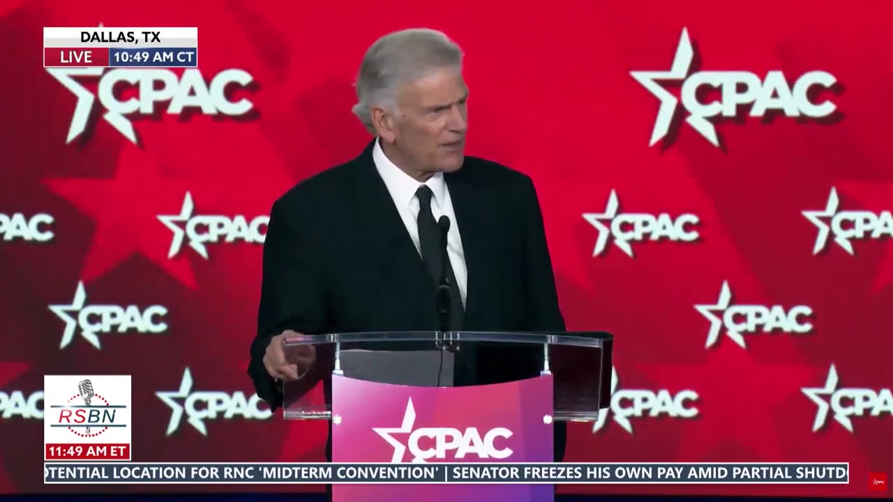 Rev. Franklin Graham speaking at a public event at a podium under stage lighting, news photography style