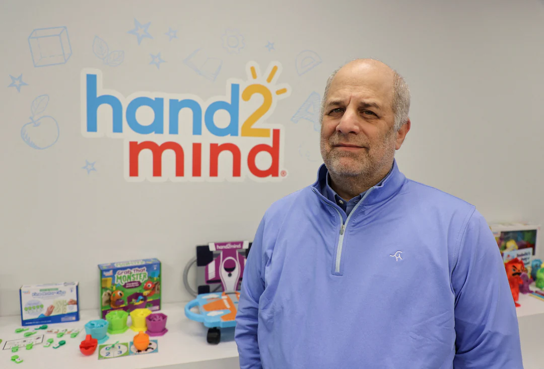 Rick Woldenberg, CEO of Learning Resources, seated at a desk in an office with paperwork and a laptop open, documentary news photograph style