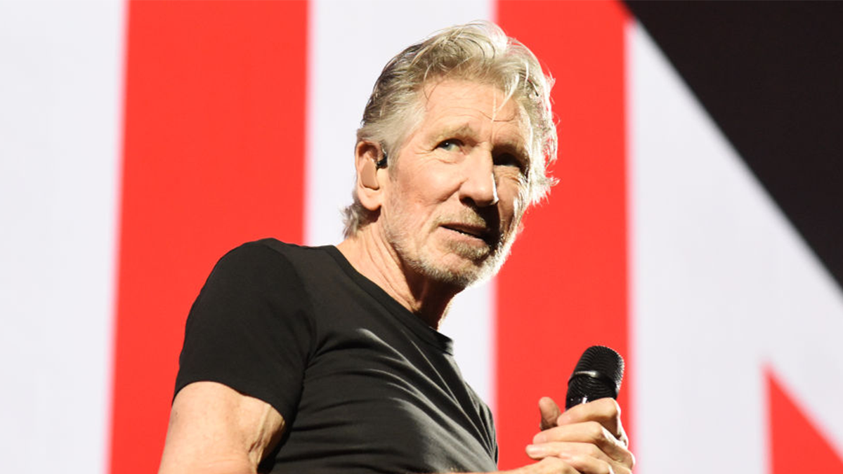 Roger Waters seated for an on-camera interview, speaking mid-sentence under studio lighting