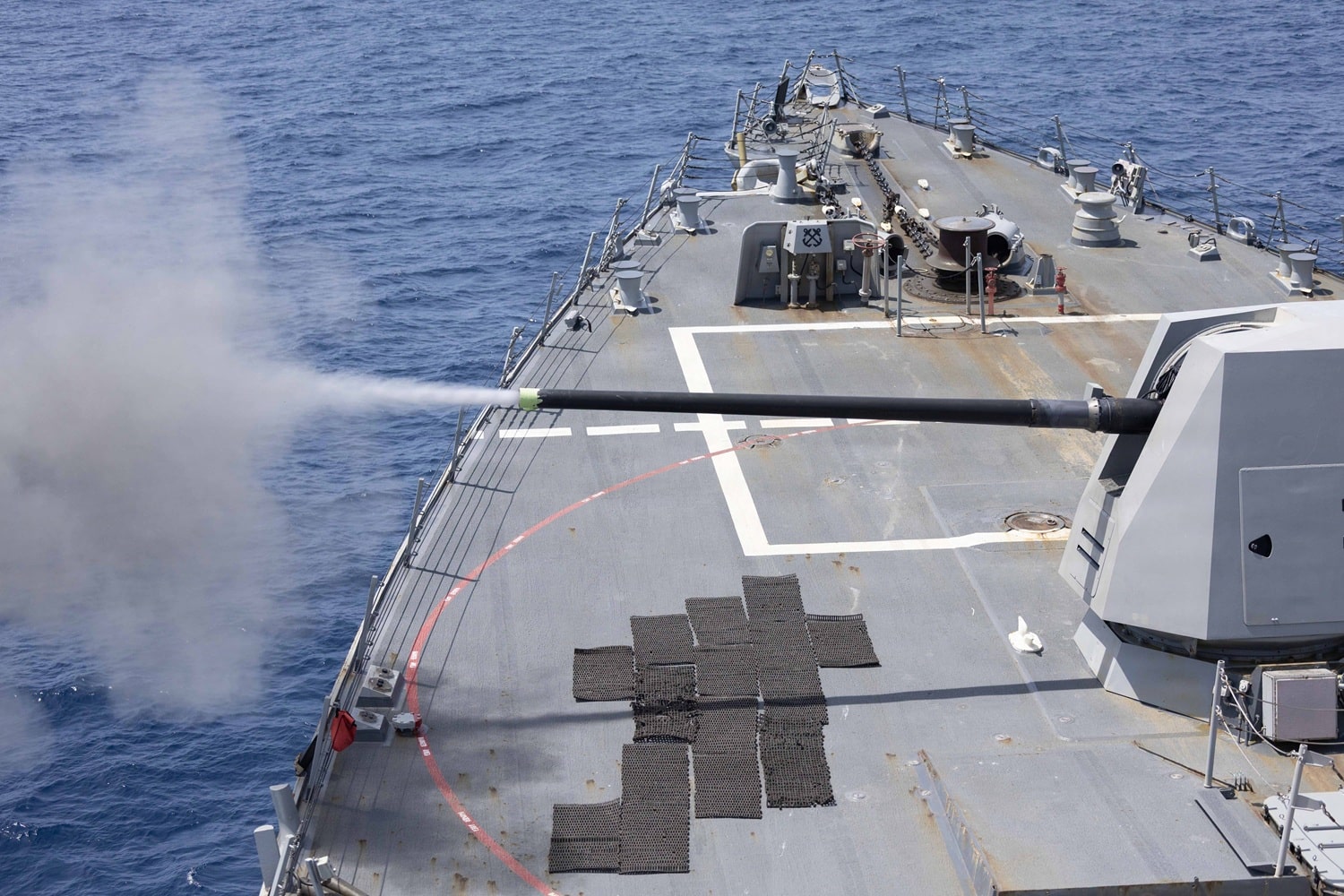 Sailors working on the deck of the USS Spruance at sea, with the ship’s superstructure and open water visible, news photography style