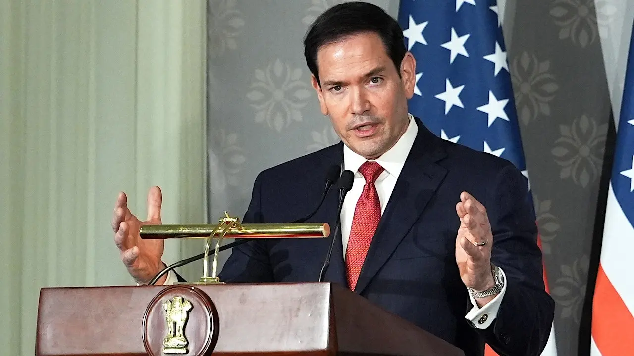 Secretary of State Marco Rubio speaking at a press conference in New Delhi, with microphones and a backdrop of officials behind him, news photography style
