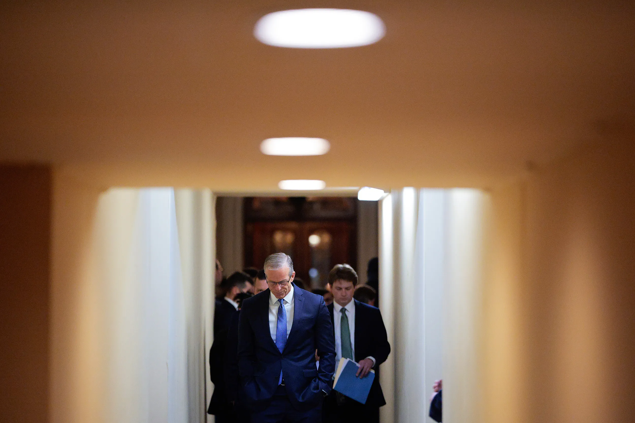 Sen. John Thune speaking to reporters in a Senate hallway with microphones extended toward him, news photography style