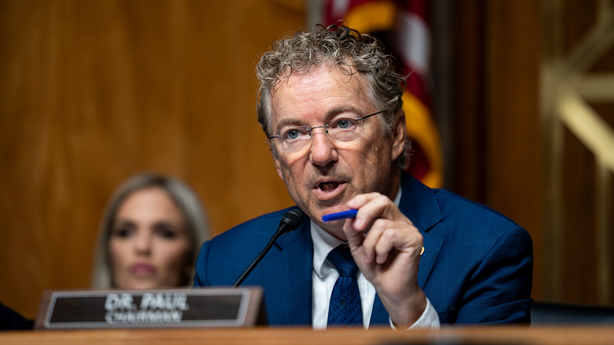 Sen. Rand Paul speaking at a Senate committee dais during a public hearing, with nameplate and microphones visible