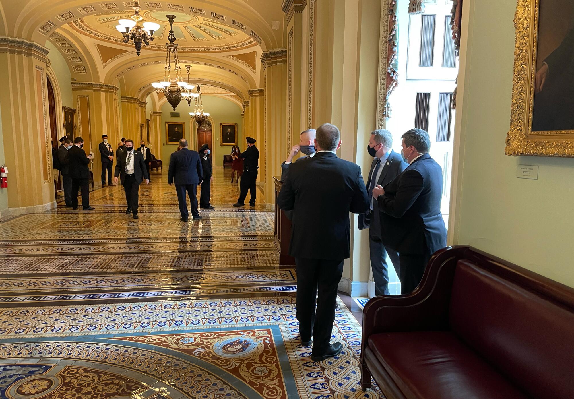 Senate staffers walking through a hallway inside the United States Capitol near the Senate side, with aides carrying folders and papers, news photography style