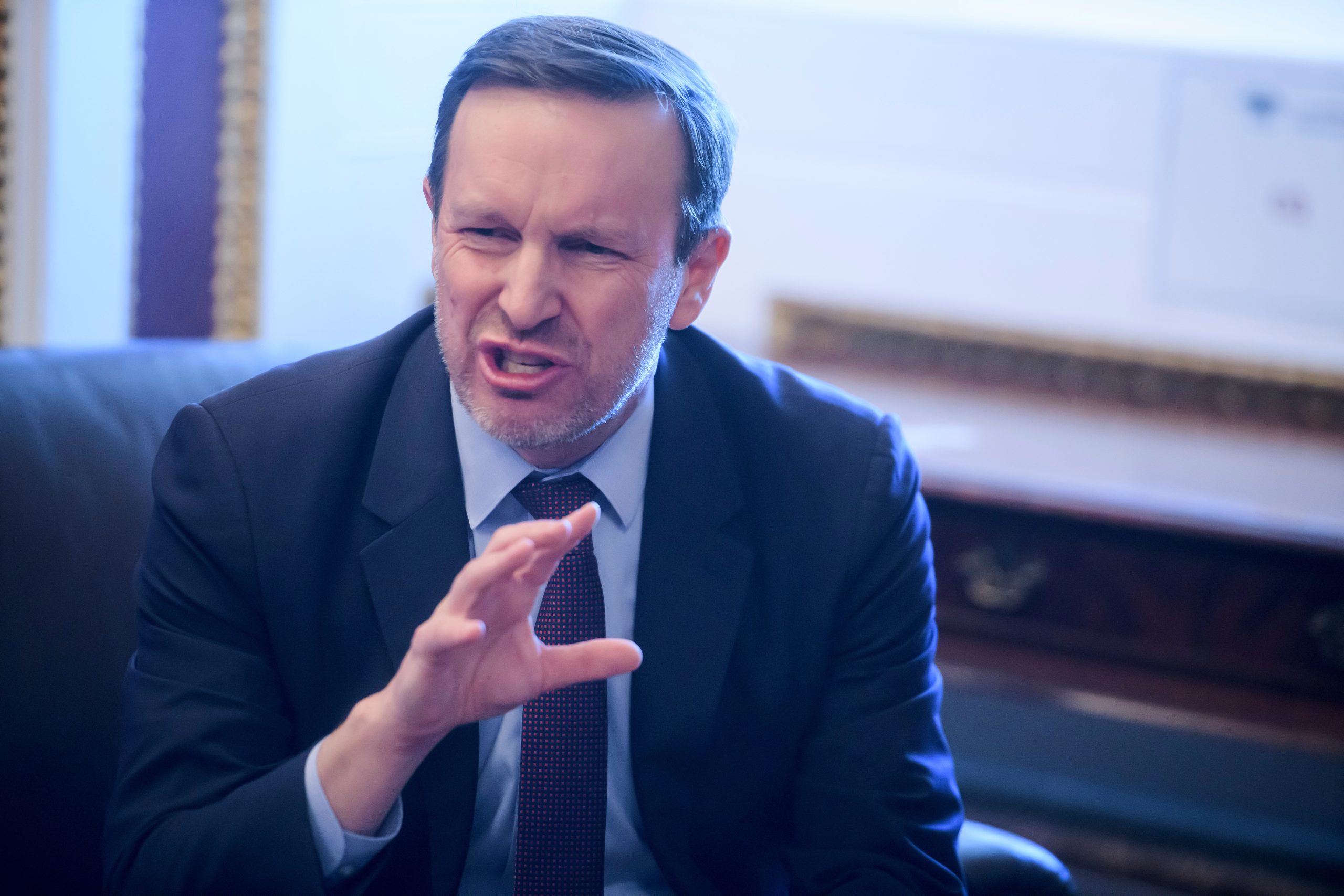 Senator Chris Murphy walking through the halls of the U.S. Capitol, photographed in a realistic news style during a period of intense political debate