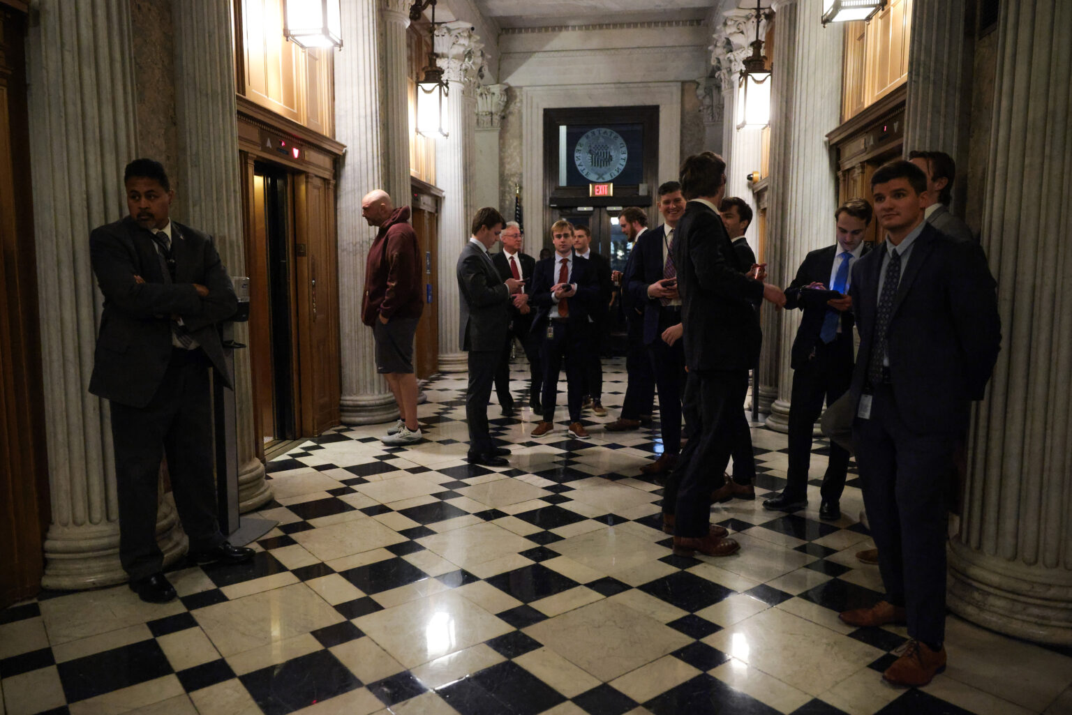 Senator John Fetterman walking through a U.S. Senate hallway in Washington, DC, wearing a dark suit and looking toward reporters, news photography style