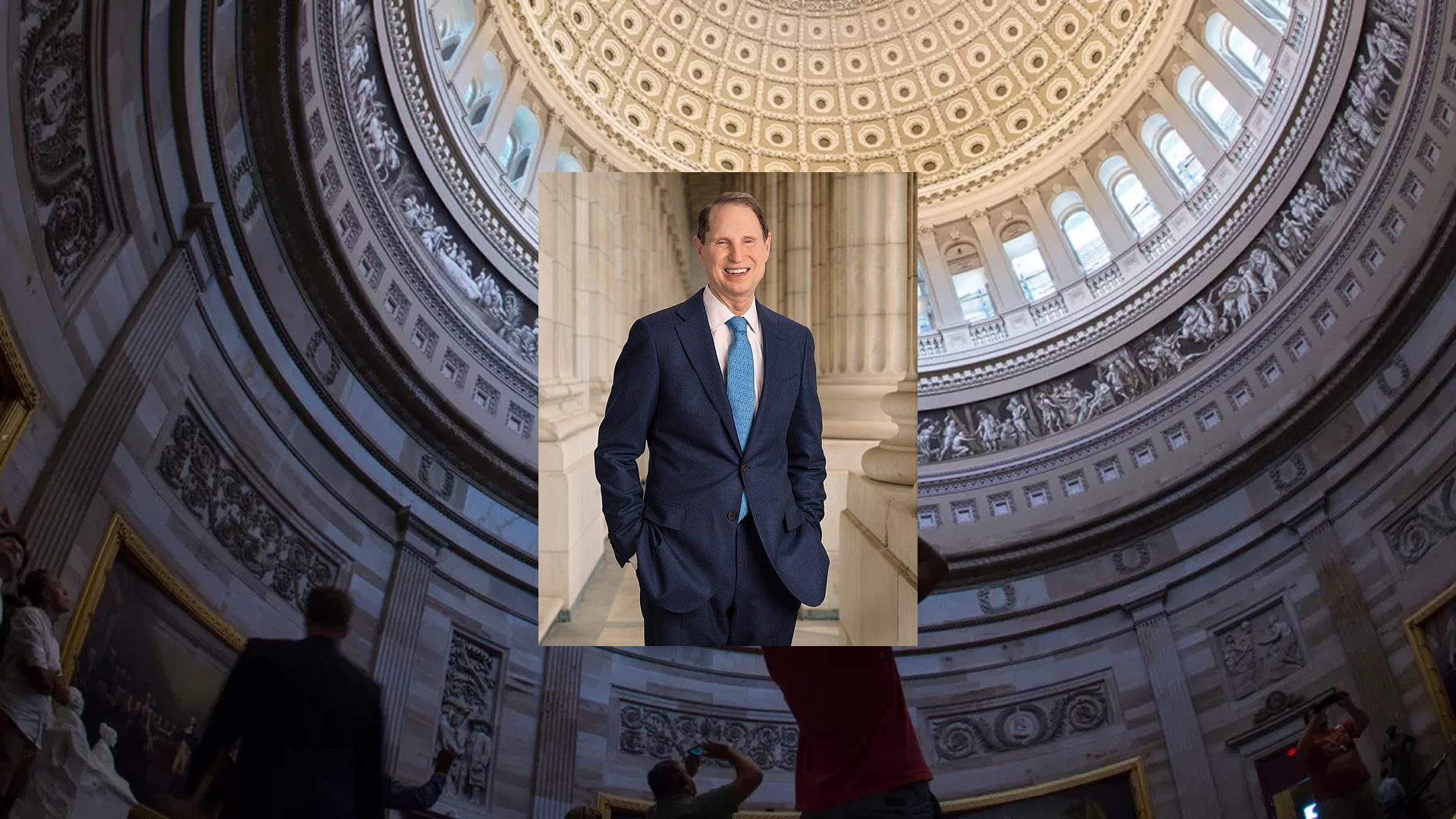 Senator Ron Wyden speaking to reporters in a hallway on Capitol Hill with microphones extended toward him, news photography style