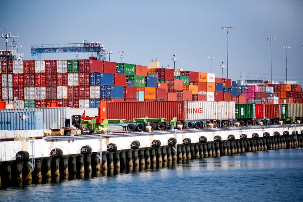 Stacks of cargo containers at a major U.S. port with cranes in the background during daytime operations, news photography style