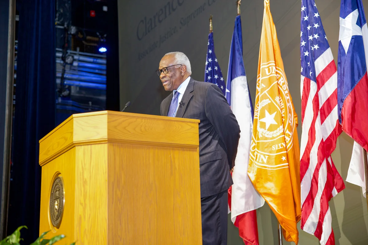 Supreme Court Justice Clarence Thomas speaking at a lectern during a university lecture in Austin, Texas, in 2026, news photography style