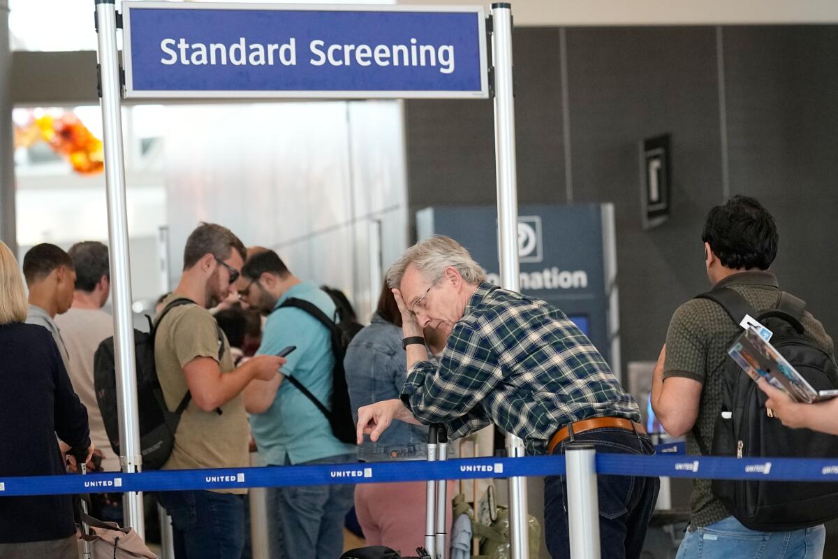 TSA officers checking passengers at a busy security checkpoint inside Los Angeles International Airport, with travelers lined up, news photography style